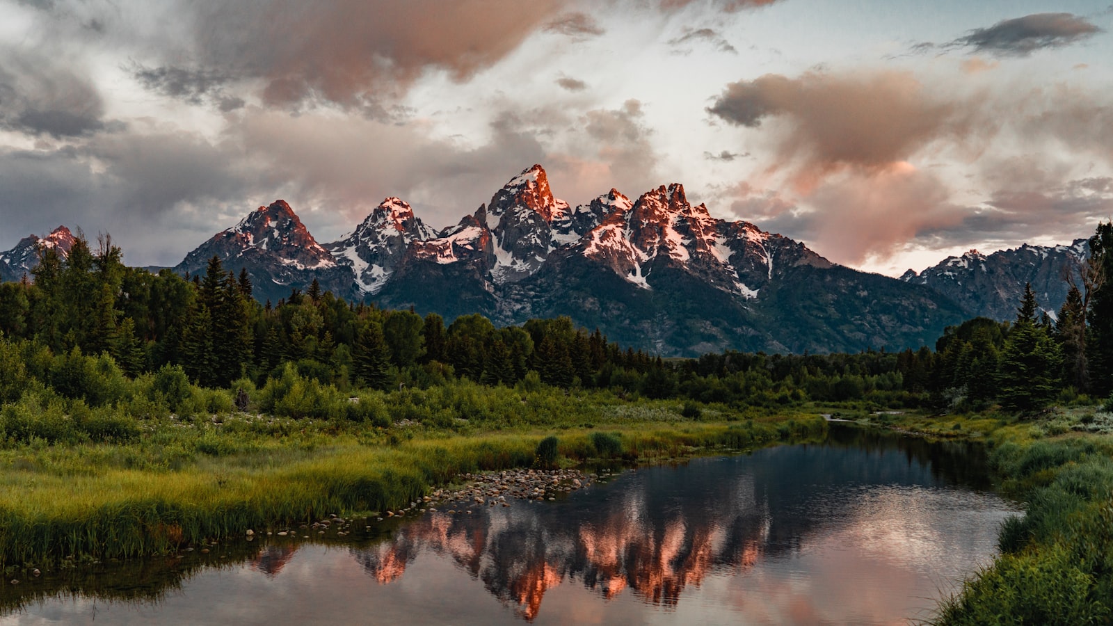 The Teton Range rising sharply behind a still alpine lake at dawn
