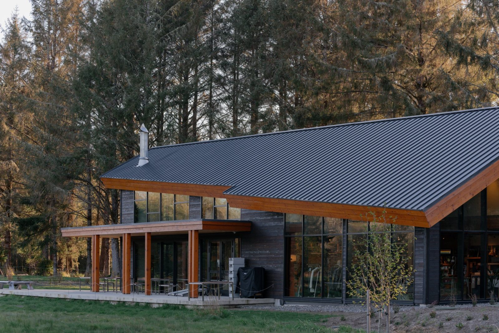 The Snow Peak Campfield Campstore in evening sun, a charred-wood building under a long dark metal roof with timber trim and tall glass walls