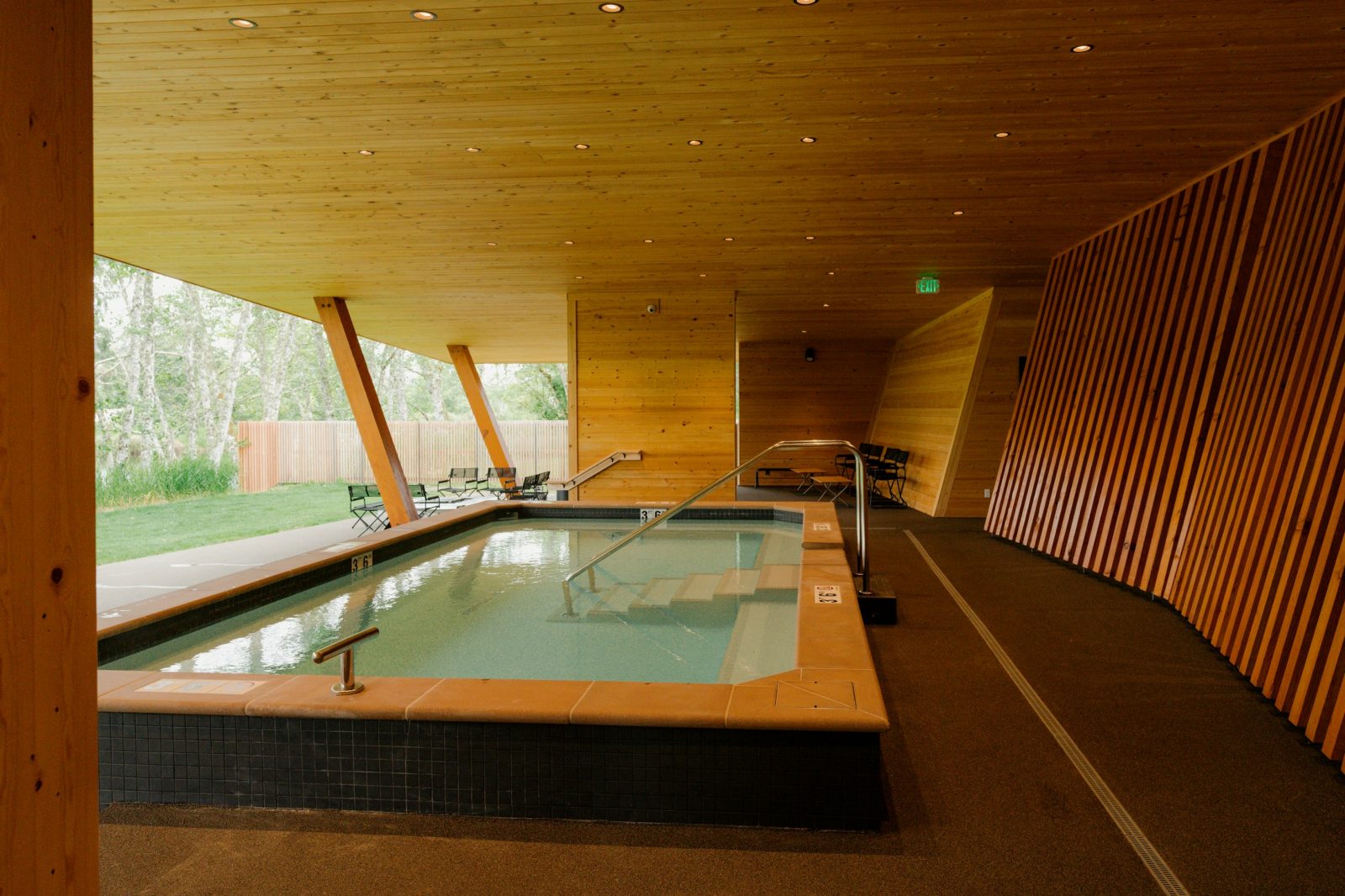 The hot soaking pool inside the Snow Peak Campfield Ofuro, a wood-rimmed pool under a timber ceiling held up by angled beams, open on one side to the grass