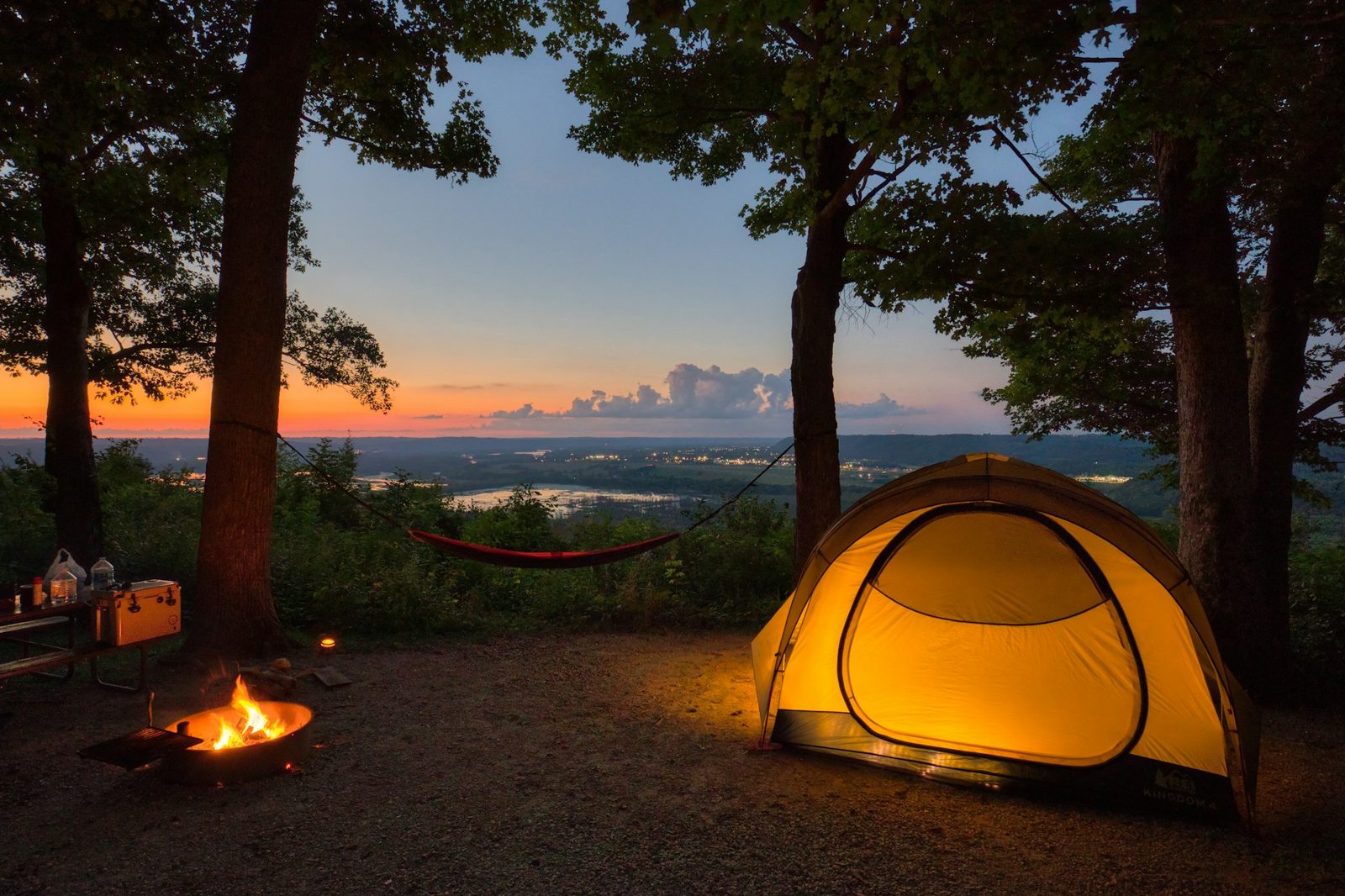 A glowing tent at dusk overlooking a river valley