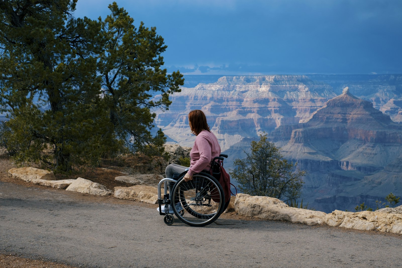 A woman in a wheelchair looks out over the Grand Canyon from a paved overlook trail