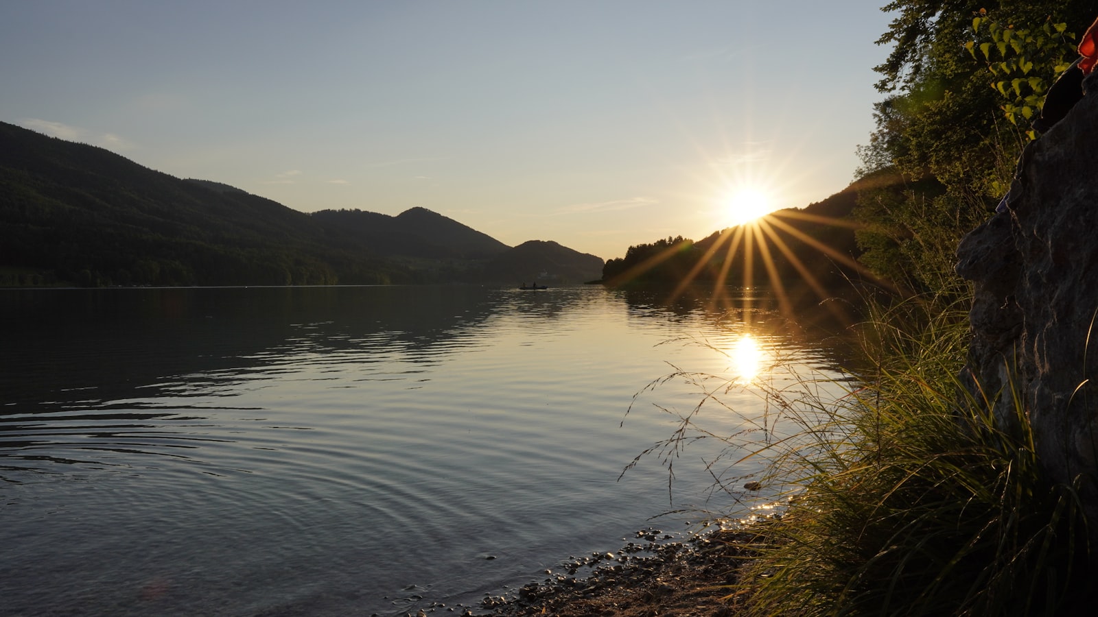 A calm lake at sunset, ringed by forested hills