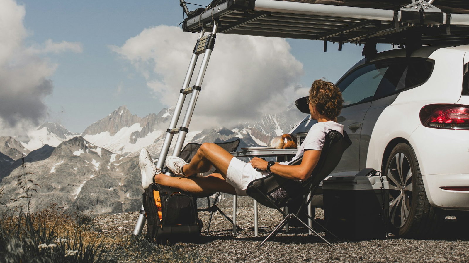 A camper sitting in bright mountain sunlight beside a car with an awning out