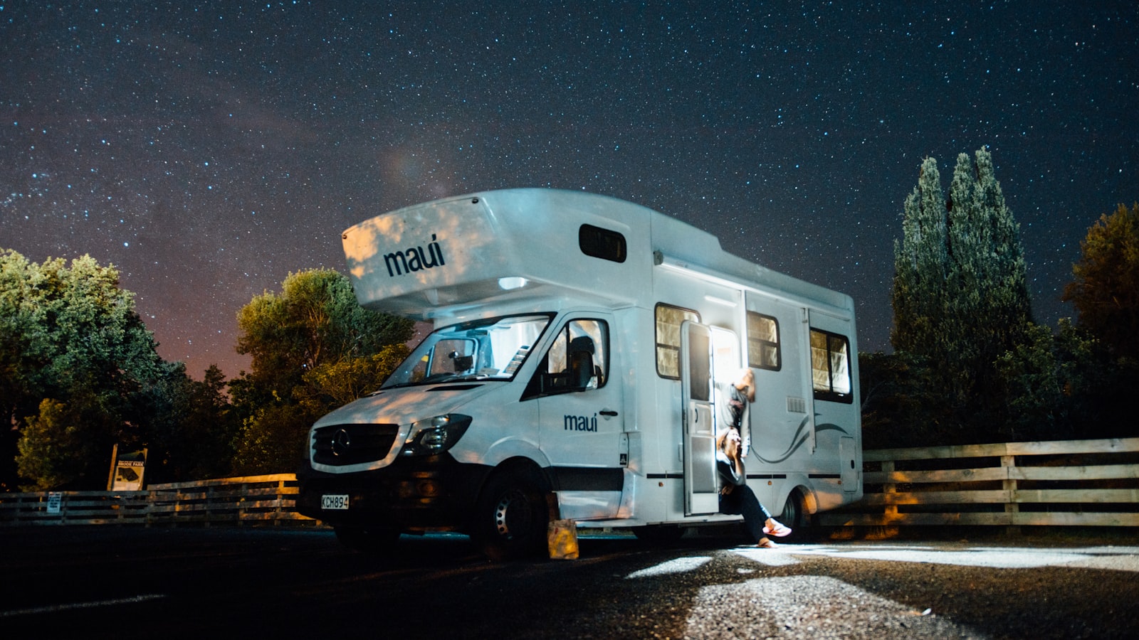 A camper van parked under a night sky full of stars, its door open and lit from inside